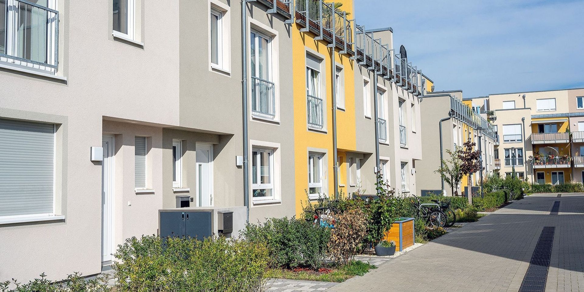 Reihenhäuser in moderner Architektur mit bunten Fassaden und bepflanztem Gehweg in Wohnsiedlung